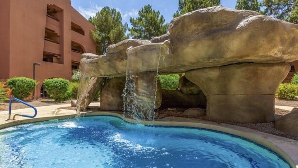 Una piscina con cascata, circondata da formazioni rocciose e un edificio con balconi.