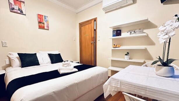 A hotel room with two beds, a wooden floor, a white table with a potted plant, and a door with a handle. - harrison motel (Auckland)
