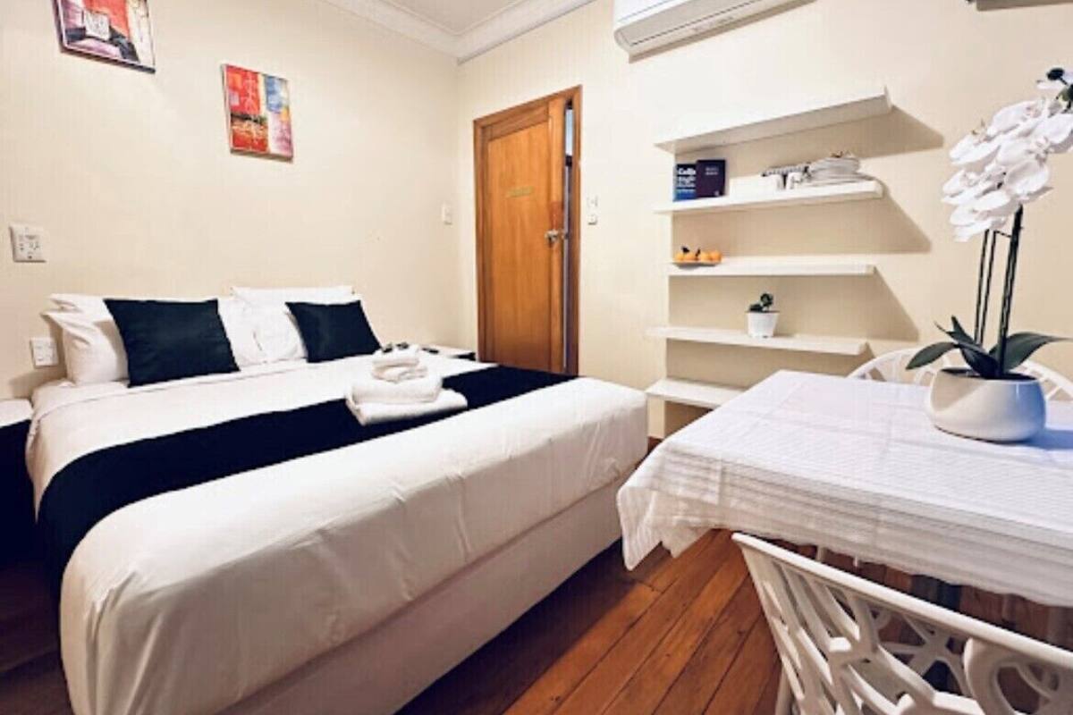 Une chambre d’hôtel avec deux lits, un plancher en bois, une table blanche ornée d’une plante en pot et une porte dotée d’une poignée.