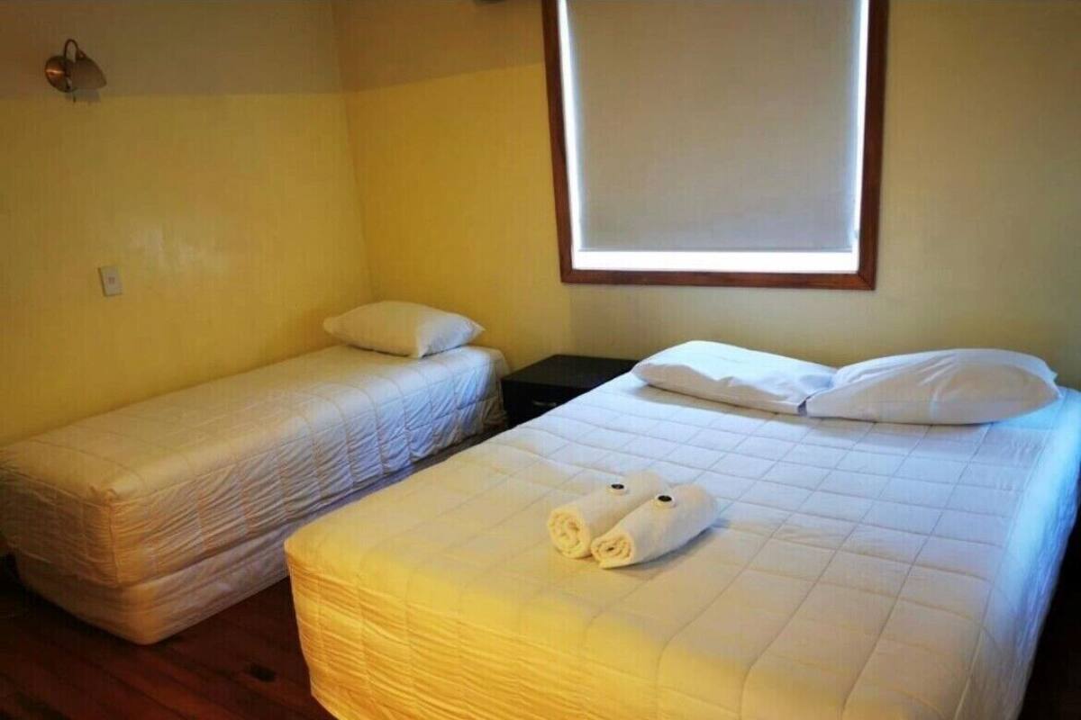 Une chambre avec deux lits, dont un plus grand et un plus petit, tous deux dotés de draps et d’oreillers blancs.