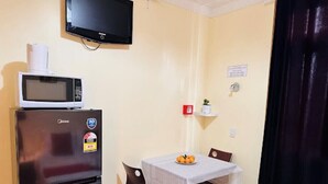 A compact room with a kitchenette, a dining table with chairs, a flat-screen TV mounted on the wall, and a small shelf with a plant. - harrison motel (Auckland)