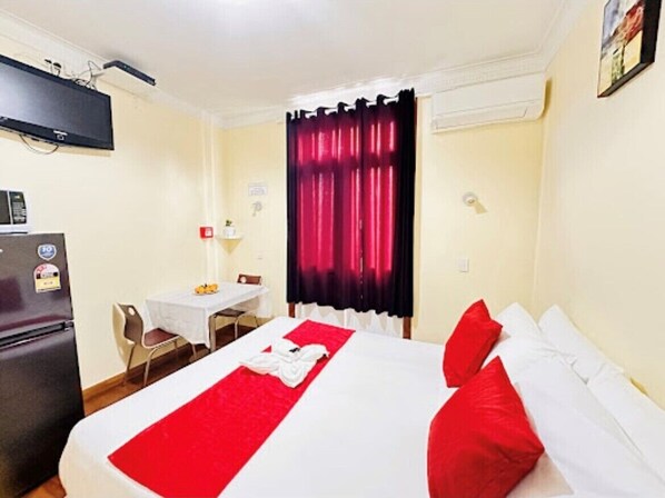 Habitación de hotel con cama, una mesita, una silla, refrigerador y ventana con cortinas.