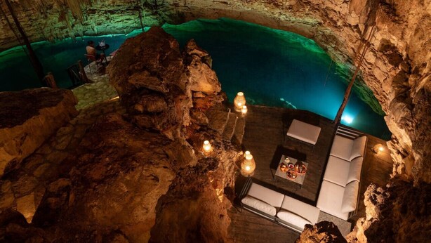 L’intérieur d’une grotte aménagée avec un espace repas, une piscine et des formations rocheuses naturelles.