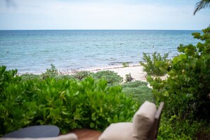 A beach view with a wooden deck and chairs, surrounded by greenery. - Beachfront Villa - Padel & Glamping at LAHOS (Chicxulub)