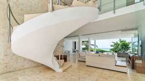 Un interior modern amb una escala espiraltra, una zona d'estar ampla amb un sofà, i vistes a l'exterior.