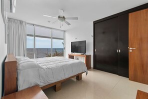A bedroom with a bed, a TV, a wardrobe, and a view of the sea. - Beachfront Villa - Padel & Glamping at LAHOS (Chicxulub)