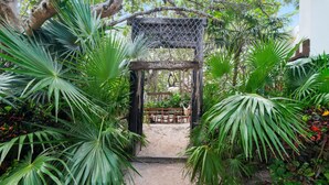 Un jardí amb una pèrgola de fusta, amb el lema "TULVICETO" i una taula amb cadires sota.