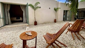 An outdoor seating area with wooden chairs and a table, surrounded by gravel, with a building in the background and a palm tree to the right. - Casa Verde Maya Downtown by LAHOS (Mérida)