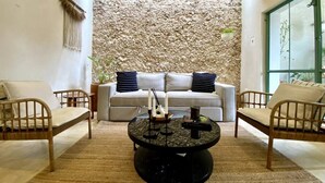 A living room with a sofa, two armchairs, a coffee table, and a stone wall. - Casa Verde Maya Downtown by LAHOS (Mérida)