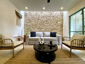 A living room with a sofa, two armchairs, a coffee table, and a stone wall. - Casa Verde Maya Downtown by LAHOS (Mérida)