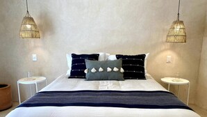 A bed with a white and navy striped blanket, two bedside tables, and two hanging lamps. - Casa Verde Maya Downtown by LAHOS (Mérida)
