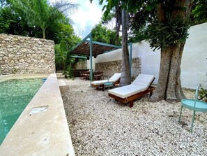 Un espace piscine comprenant des chaises longues, une pergola et un mur en pierre.
