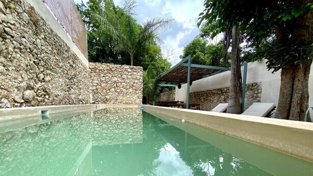 A swimming pool with a stone wall and a covered area with chairs. - Casa Verde Maya Downtown by LAHOS (Mérida)