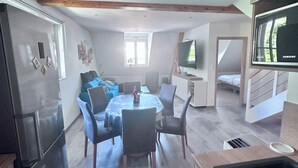 Una cucina moderna con frigorifero integrato, un'area pranzo con tavolo rotondo e sedie, un divano blu e una televisione a parete.