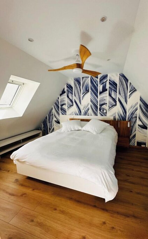 A bedroom with a bed, wooden floor, ceiling fan, and leaf-patterned wallpaper. - Duplex hyper center parking (Haguenau)