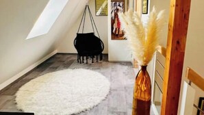 Camera da loft moderna con un'ampia finestra a lucernario, un tappeto bianco e soffice, una poltrona sospesa e un vaso con pampas.