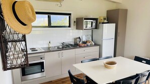 A compact kitchen with a microwave, refrigerator, and oven. There is a dining table with chairs and a basket on it. - Delatitie Apartments -Cedar 1 Bedroom Apartment - Merrijig (Merrijig)