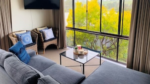 A living room with a sofa, two wicker chairs, a coffee table, and a TV mounted on the wall. - Delatitie Apartments -Cedar 1 Bedroom Apartment - Merrijig (Merrijig)