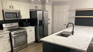 Una cocina moderna con electrodomésticos de acero inoxidable, armarios blancos y encimera de mármol.