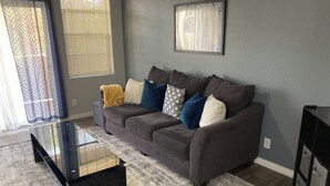 Una sala de estar moderna con un sofá gris, almohadones estampados, una mesa de centro negra y una alfombra gris.