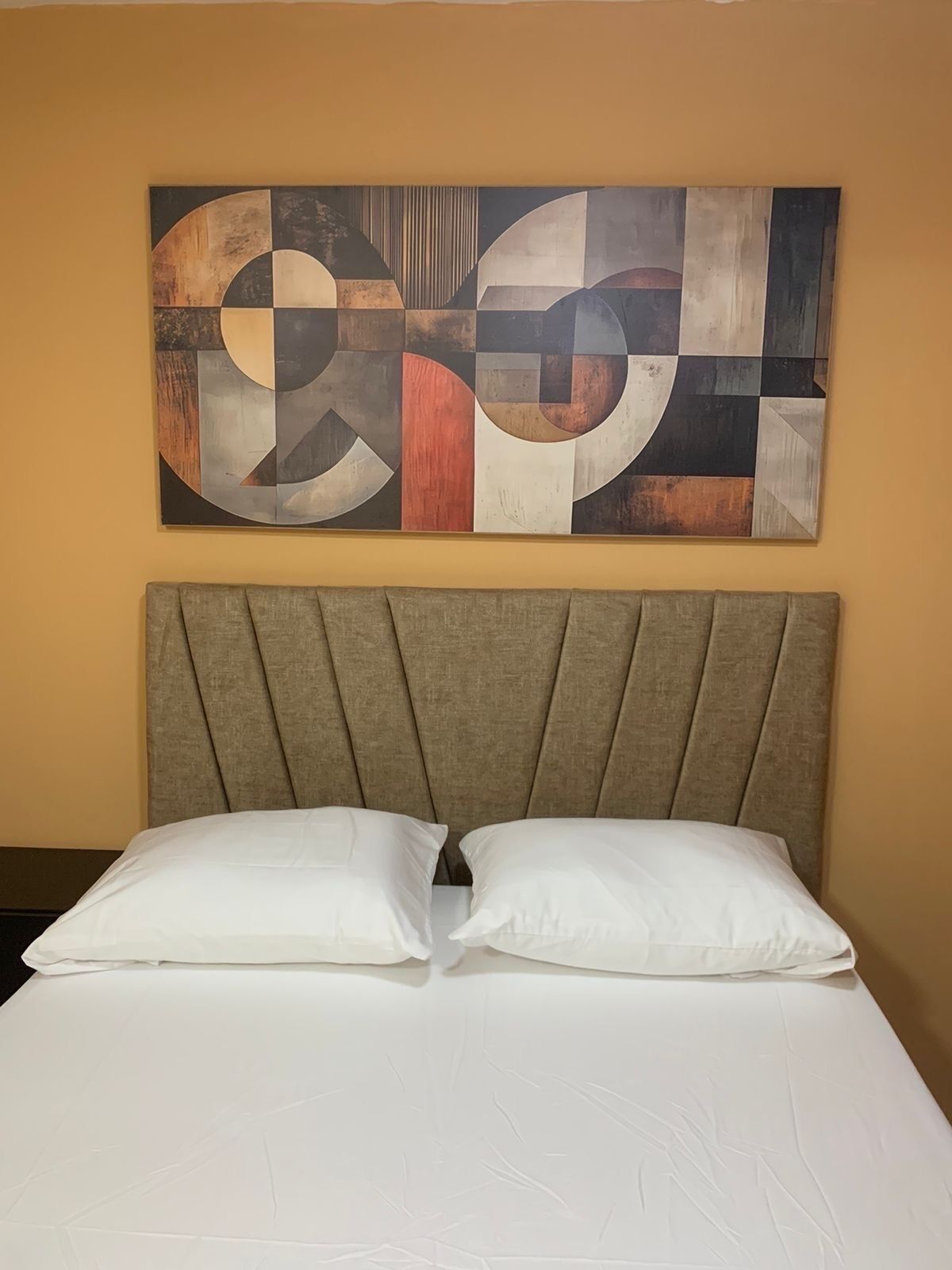 Una cama con cabecera y un cuadro abstracto grande sobre ella.