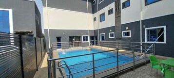 Piscina interior moderna con barandilla metálica, rodeada por un edificio con múltiples ventanas y una escalera.