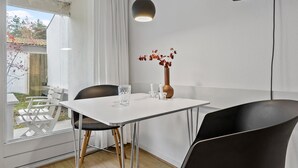 Un espace de salle à manger moderne avec une table blanche, des chaises noires, un vase de fleurs et une suspension.