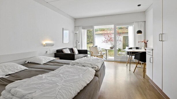 Une chambre d’hôtel moderne avec deux lits, un bureau et un balcon donnant sur un jardin et une maison.