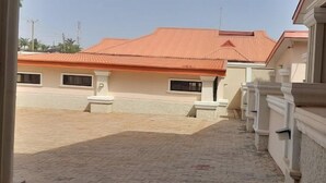 A building with a red roof and white walls, featuring a paved courtyard and a series of columns along the right side. - Mayo Premium Inn (Kaduna)