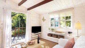 Una sala de estar acogedora con televisor, una mesa de centro de madera, sofá y un balcón con vista a la vegetación.