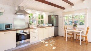 Una cocina con armarios blancos, encimera de madera, horno integrado, microondas, campana extractora de acero inoxidable, refrigerador y una mesa de comedor con sillas.