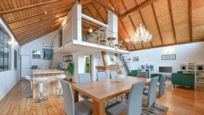 A spacious loft-style living area with a high ceiling, wooden beams, a dining table with chairs, a staircase to an upper level, and a chandelier. - Beautiful home in Falinic Breg with sauna (Falinic Breg)