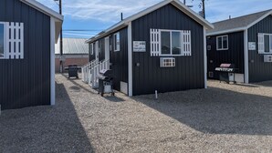 A row of small, dark-colored cabins with white-framed windows and a gravel ground. Each cabin has a sign with a number and contact information. - The CB&M Myton Minis  (Myton)