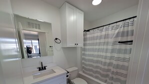 A modern bathroom with a white vanity, a toilet, and a shower with a striped curtain. - The CB&M Myton Minis  (Myton)