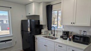 A compact kitchen with white cabinets, a black refrigerator, a microwave, and a coffee maker. - The CB&M Myton Minis  (Myton)