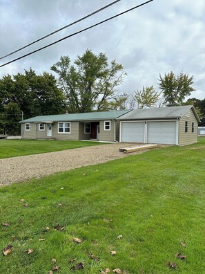 A single-story house with a garage, a front yard with a gravel path, and a lawn with scattered leaves.