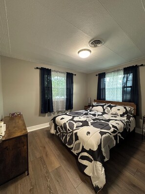A bedroom with a large bed, wooden flooring, and a nightstand.