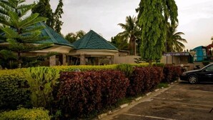 A building with a green roof, surrounded by well-maintained hedges and palm trees. - Zecool Hotels (Kaduna)