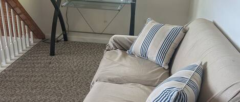 A room with a beige sofa, striped pillows, a glass coffee table, and a window with blinds.