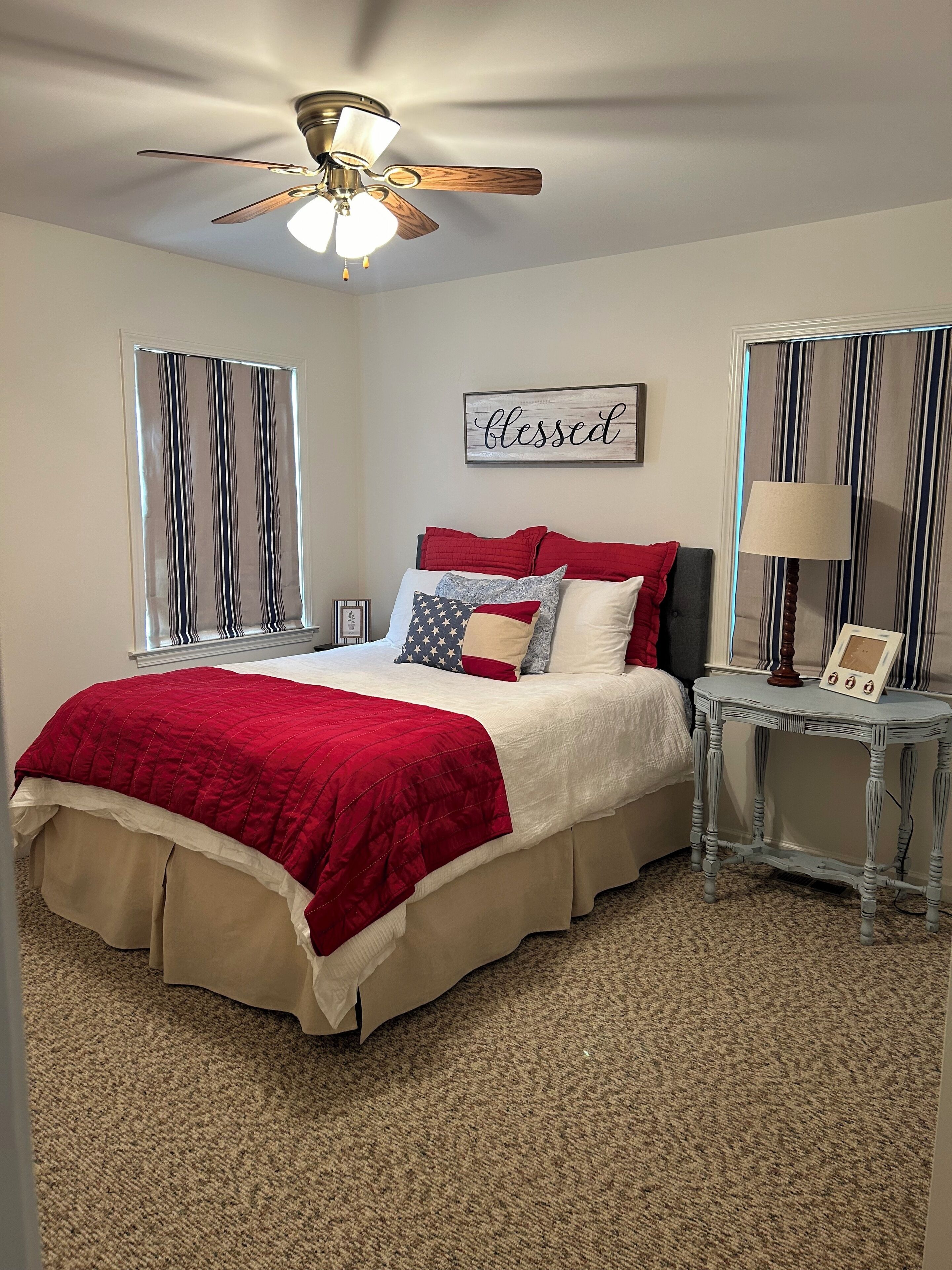 Une chambre à coucher avec un lit, un ventilateur de plafond, une table de chevet avec une lampe et une fenêtre avec des stores.