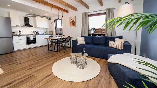 Una sala de estar moderna con un sofá azul, una mesa de centro redonda y una zona de comedor con una mesa y sillas.