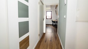 Un pasillo con piso de madera, paredes blancas y una zona de comedor con mesa y sillas.