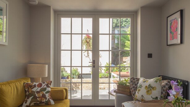 Un salon avec un canapé jaune, une table et une vue sur un espace extérieur verdoyant, accessible par une porte vitrée.