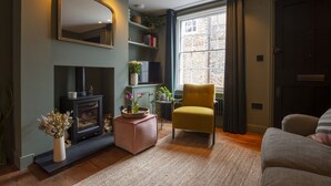 Un salon chaleureux avec une cheminée, un fauteuil confortable et une grande fenêtre agrémentée de rideaux.