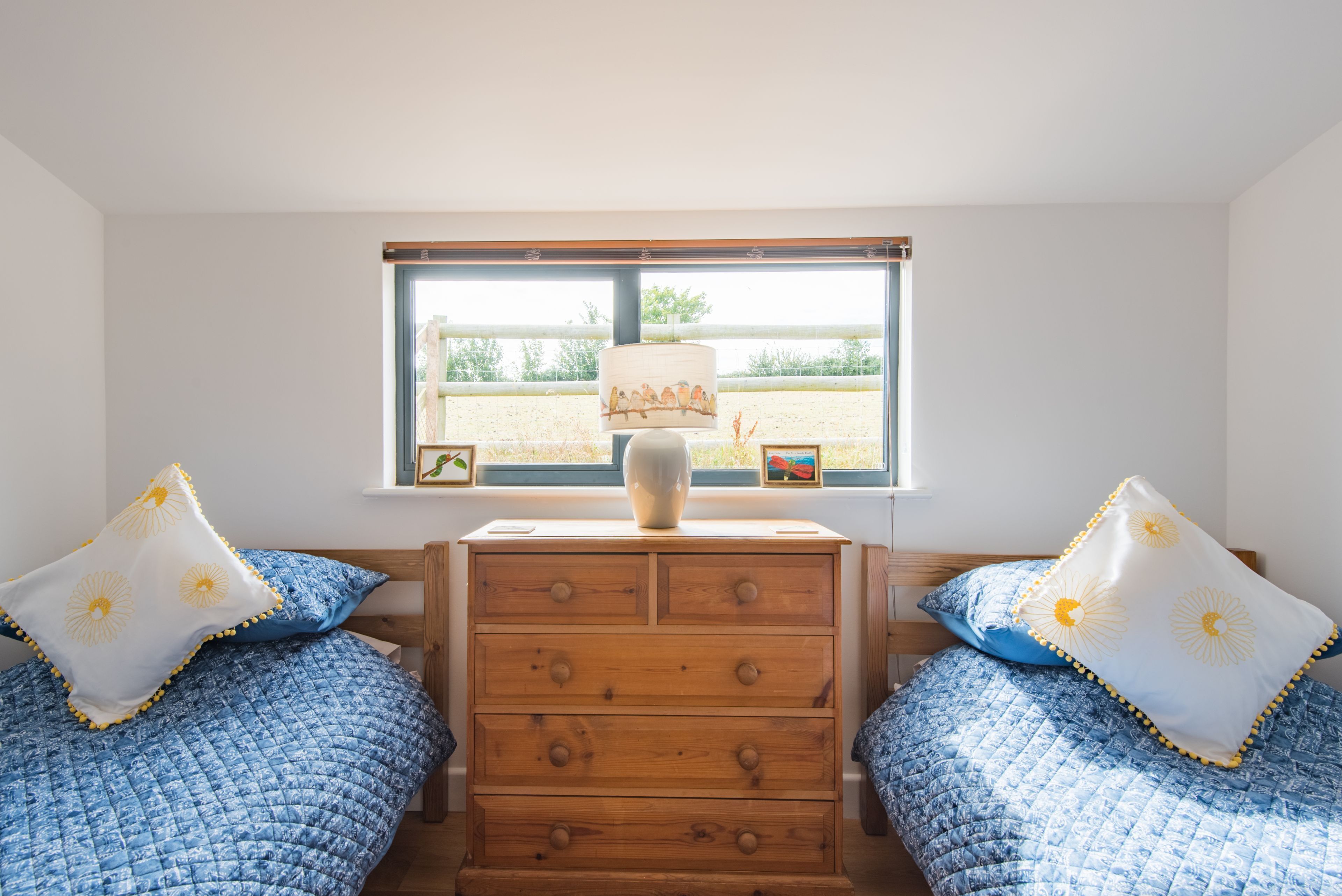 Un dormitorio con dos camas, un aparador de madera, una ventana con vista a la playa y una lámpara en el aparador.