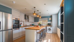 A modern kitchen with stainless steel appliances, a central island with stools, and a washing machine. - Sea to Sea, Hythe Kent (Hythe)