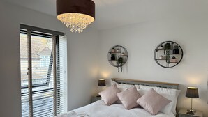 Une chambre à coucher comprenant un lit, deux tables de chevet, un lustre suspendu et deux étagères à plantes fixées au mur.