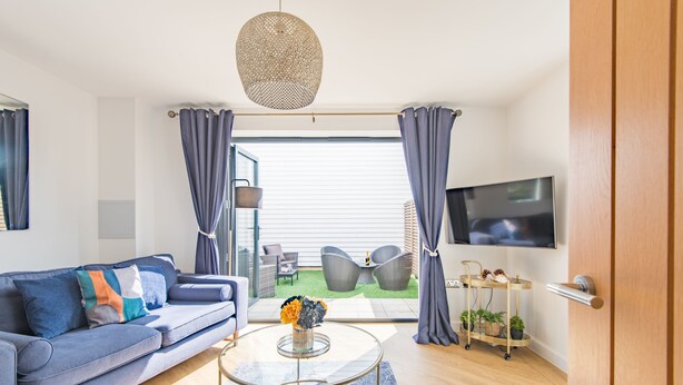 Un salon moderne avec un canapé, une table basse et un téléviseur. Il y a un balcon aménagé avec du mobilier d’extérieur.
