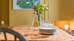Una mesa de comedor con una botella de vino, un florero con flores y platos apilados.