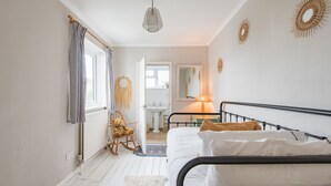 Un dormitorio con una cama, una mecedora, una mesita de noche, una lámpara y una ventana con cortinas.